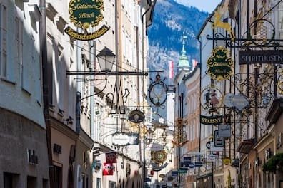 Getreidegasse in der historischen Altstadt, zahlreiche hohe Bürgerhäuser aneinandergereiht mit schmiedeeisernen Zunftzeichen Salzburg