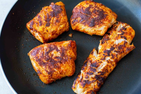 Four cooked seasoned white fish fillets in a skillet.