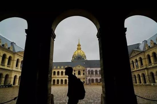 在淅淅沥沥的小雨中，法国军事博物馆游客稀少，而且部分建筑正在维修中，单纯地拍摄建筑意思不大。等待一名游客从镜头前走过时释放快门拍摄，由于按照背景亮度测光、曝光，所以环廊中走过的人物形成了剪影。剪影状态的人物既能够活跃画面，又可以避免肖像权纠纷。何乐而不为？使用索尼A7RII及Vario-Tessar T FE24-70mmF4 ZA OSS镜头拍摄，感光度ISO 250。光圈F8，速度1/400秒。