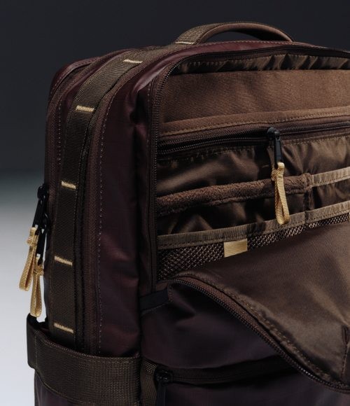A brown backpack with the zipper open, showing its organizational compartments. 