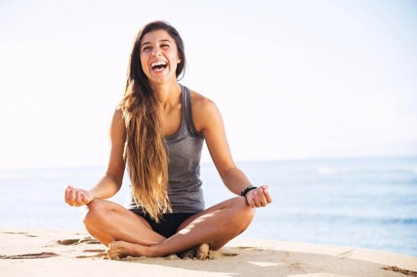 A happy woman sitting by the ocean.