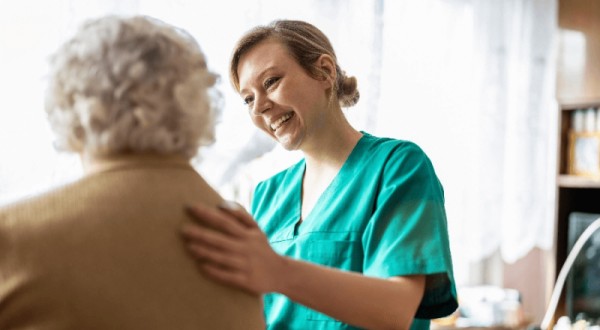 Female nurse in green uniform supporting elderly patient