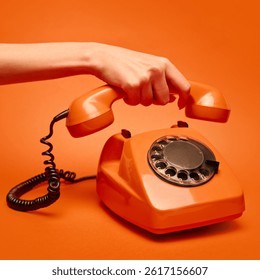 一只手拿起一部老式橙色转盘电话的听筒，背景也是橙色的。体现了复古、怀旧、科技和波普艺术的概念。适用于创意视觉设计、海报等。