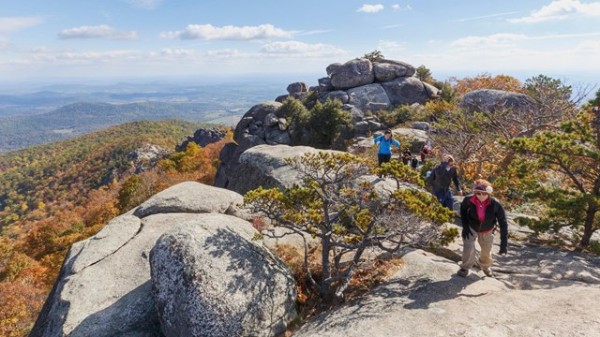 A large group of people hiking on a mountain top full of boulders and rocks.