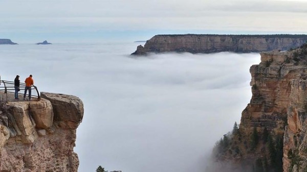 two people at a scenic overlook are looking at a vast canyon filled with a cloud inversion. 