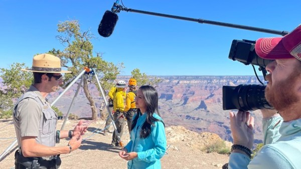 A ranger is interviewed near the canyon rim with a reporter and a videographer. 