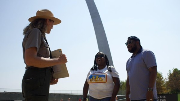 A park ranger standing in front of the arch holding pictures, talking to a couple.