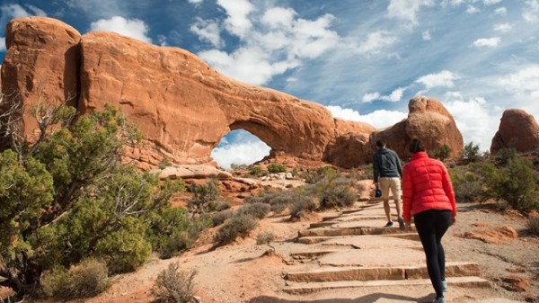 Two people walking up a set of steps on a trail leading to an arch.
