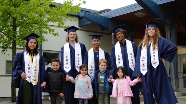 Five graduates of Lindbergh High School in Renton pose in their gowns with Kindergarteners from the school district