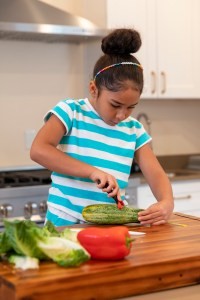 一个穿着鲜艳条纹T恤的7岁男孩在厨房里削黄瓜。