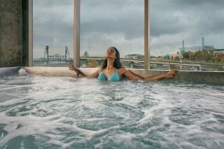 A woman relaxes in a hot tub with a view of Willamette River and bridges in the background.