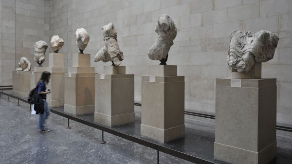 A visitor observing a collection of 7 sculptures displayed in the Duveen Gallery at the British Museum in London.