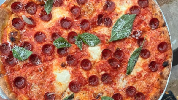 A thin-crust pizza as shown from above, topped with small pepperonis with the edges turned up, parmesan, and whole basil leaves.